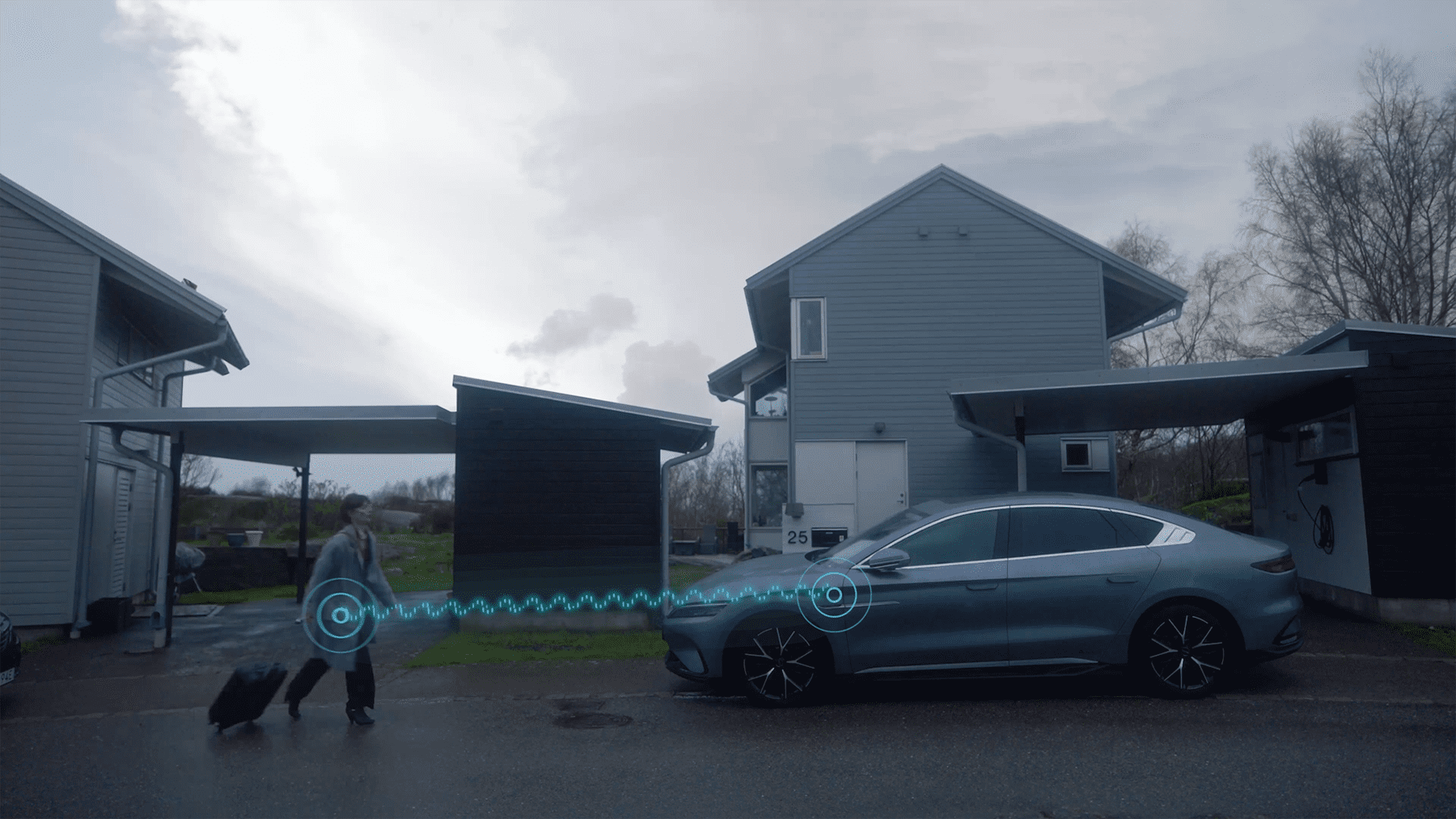 A person walking with a suitcase in front of a modern house while a digital signal graphic connects them to a nearby parked car, suggesting advanced keyless access technology.